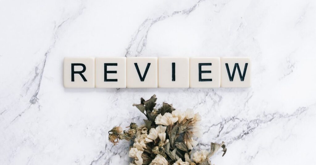 リカバリーウェアの口コミレビューをイメージした写真。大理石の背景に「REVIEW」と並ぶ木製ブロックとドライフラワー。