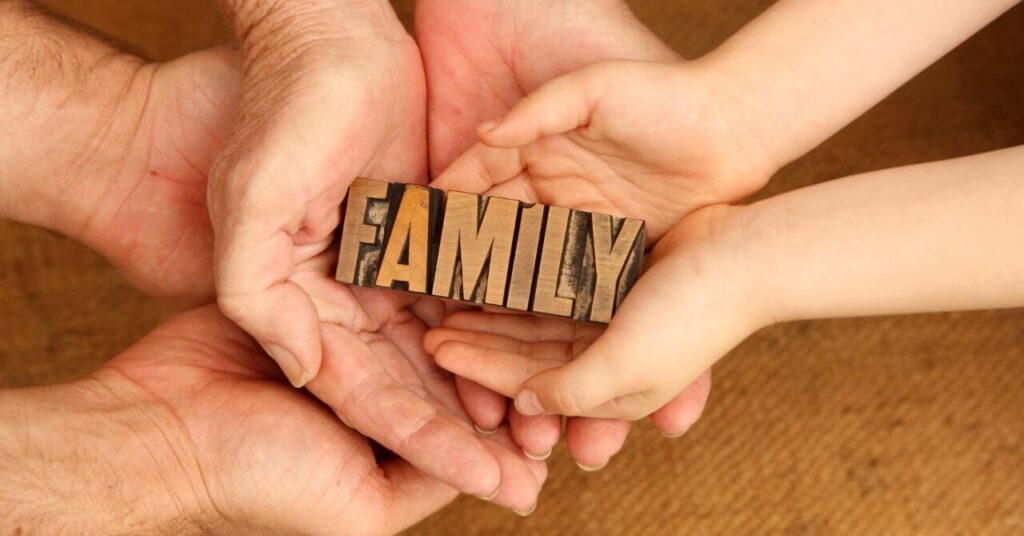 家族の手が一緒に木製の「FAMILY」の文字を支えている写真|家族にお願いするときの協力を表すイメージ