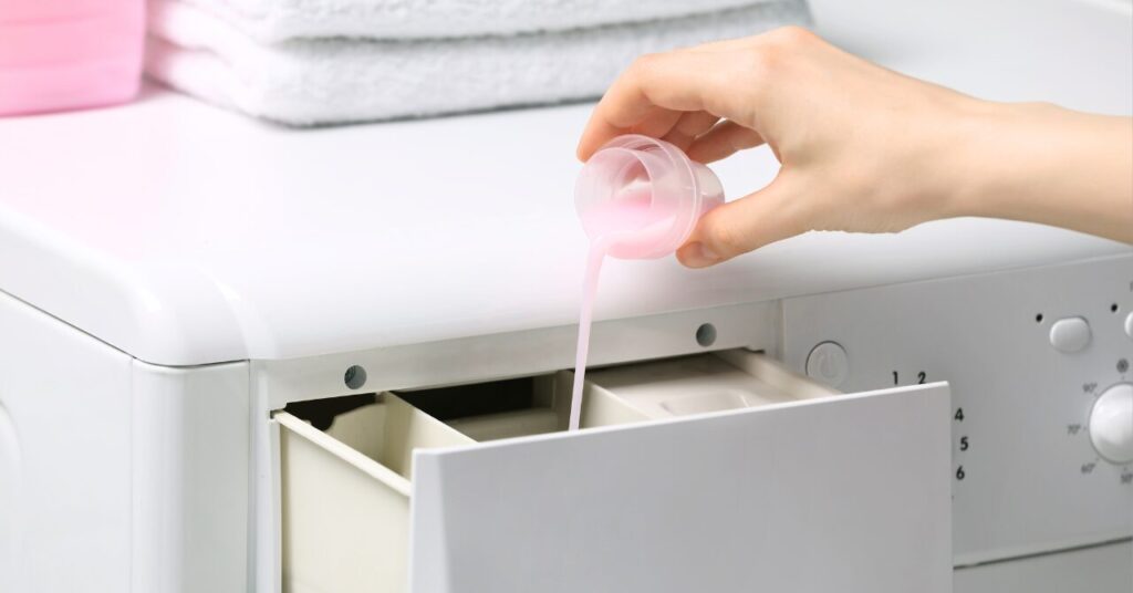 柔軟剤を計量カップから洗濯機に注いでいる手元の写真|柔軟剤を入れすぎて心配になった場合のイメージ