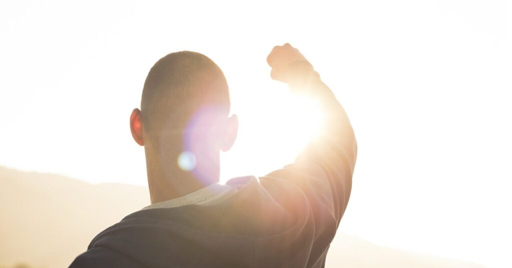 朝日を背に拳を突き上げる男性。リカバリーウェアを味方にして前向きに一歩踏み出すイメージをユーモラスかつ前向きに表現した画像。