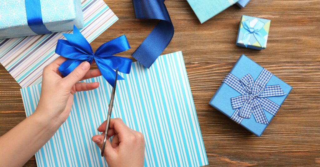青いリボンでギフトを丁寧にラッピングしている様子。贈り物に心を込めて仕上げる“ちょっとした気配り”を表現した写真。