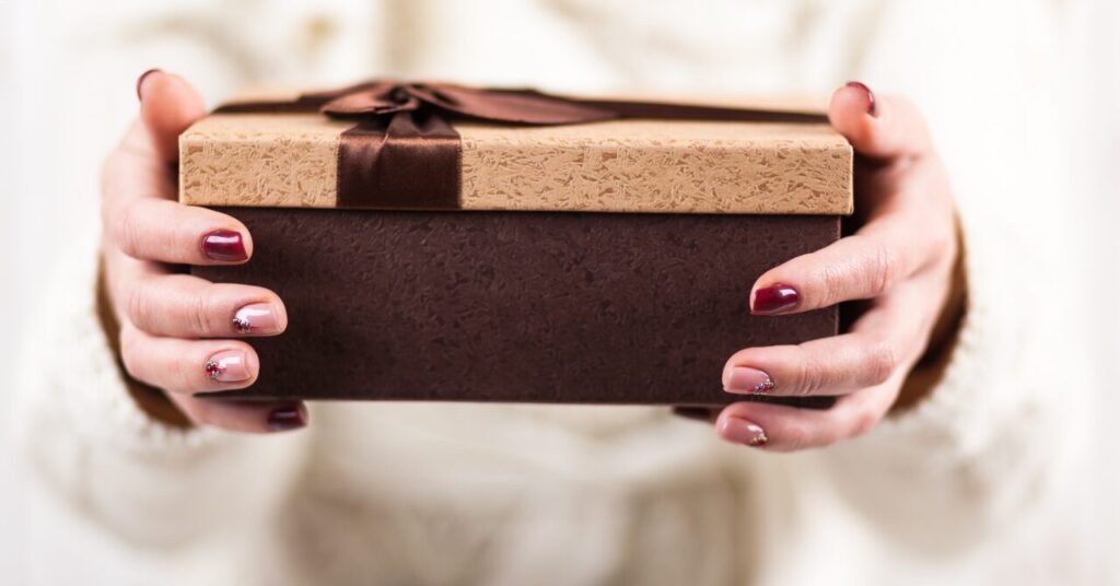 両手で丁寧にプレゼントを差し出している様子。相手の体に寄り添うような優しさと気配りを表現した写真。