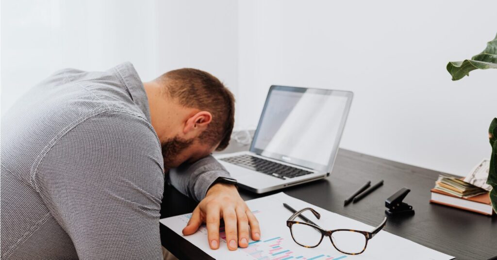 パソコンの前で疲れて机にうつ伏せになっている男性の様子。疲労でリカバリー効果を感じない状態をイメージした写真。
